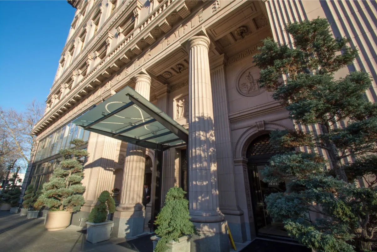 A grand exterior view of the hotel's entrance, featuring ornate columns, a glass awning, and manicured greenery. The setting captures arriving guests and offers a sense of luxury and welcome.
