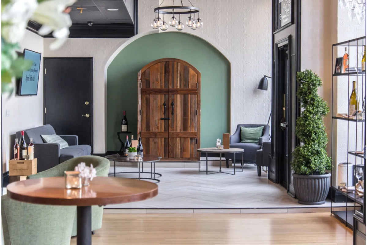 A stylish seating area set against a green accent wall, with shelves filled with bottles suggesting a wine or beverage service. The inviting arrangement and contemporary design create a boutique hotel vibe, ideal for socializing or enjoying a drink.