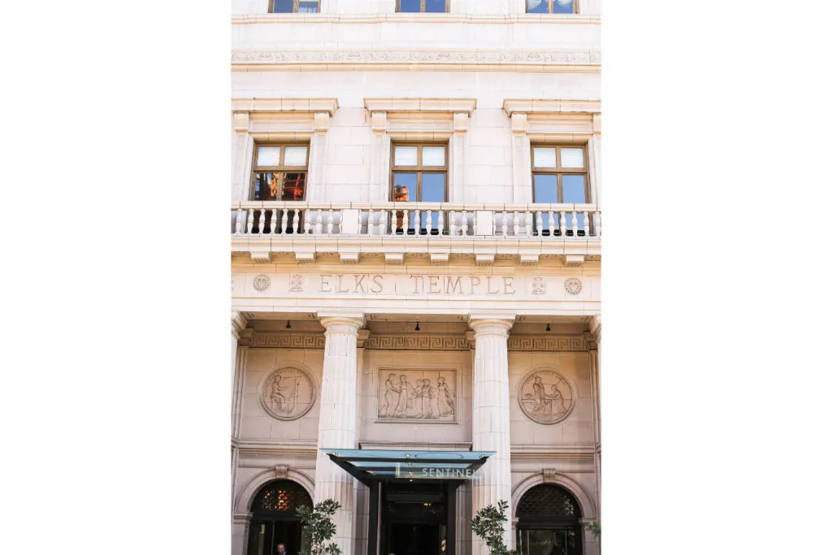 A stately exterior shot highlighting the Elks Temple’s signage, decorative architectural columns, and historic stone reliefs. The setting is elegant and inviting, with hints of community gatherings or tours.