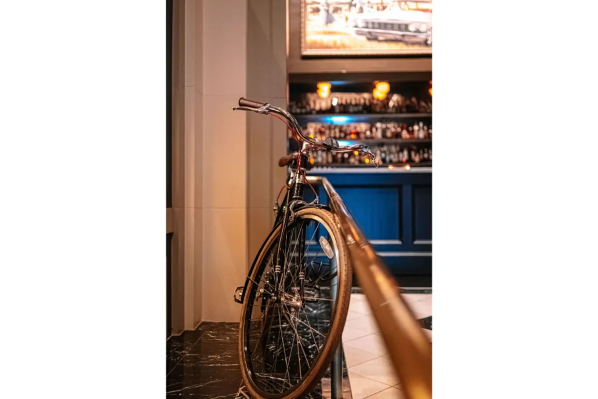 This image captures a bicycle prominently displayed near a stylish bar counter, with warm lighting creating a relaxed and nostalgic atmosphere. The interior nods to an active lifestyle, blending the idea of cycling with socializing after a day of adventure.