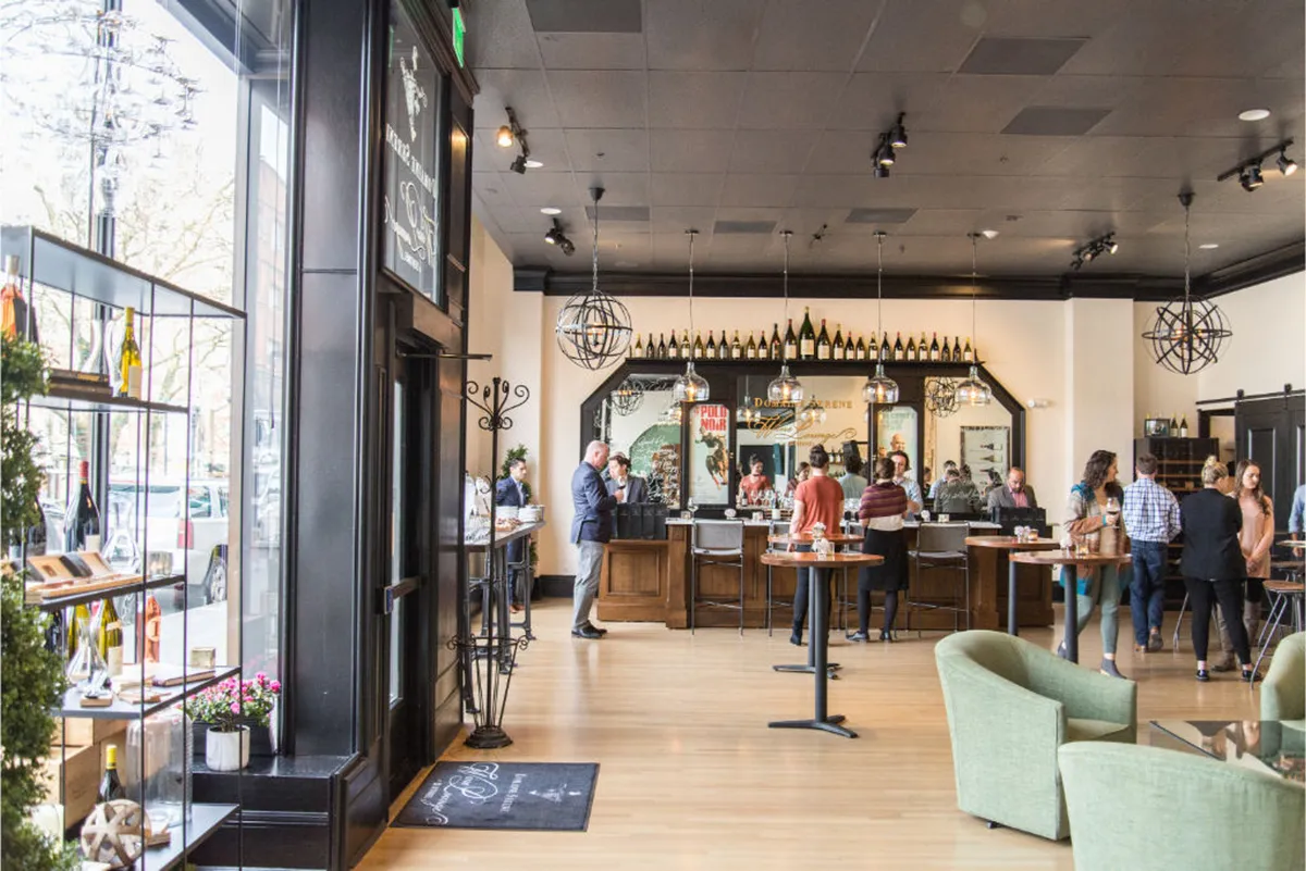 A lively wine bar area with a well-stocked wine display, comfortable seating, and guests enjoying tastings and conversation. The ambiance is vibrant, reinforcing the idea of daily social events and hospitality.